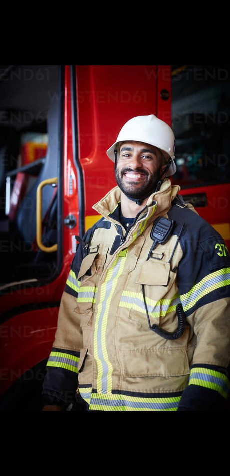 portrait of smiling male firefighter standing against fire engine at fire station masf14201